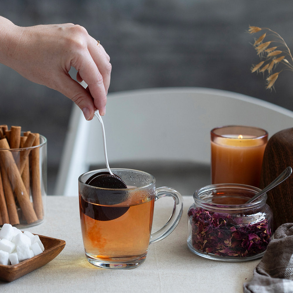 Person dippin' the cookietea infuser in a glass mug