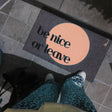 Doormat with 'be nice or leave' text on a tiled floor