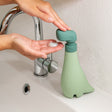 Person using the Soapasaurus soap dispenser on a sink